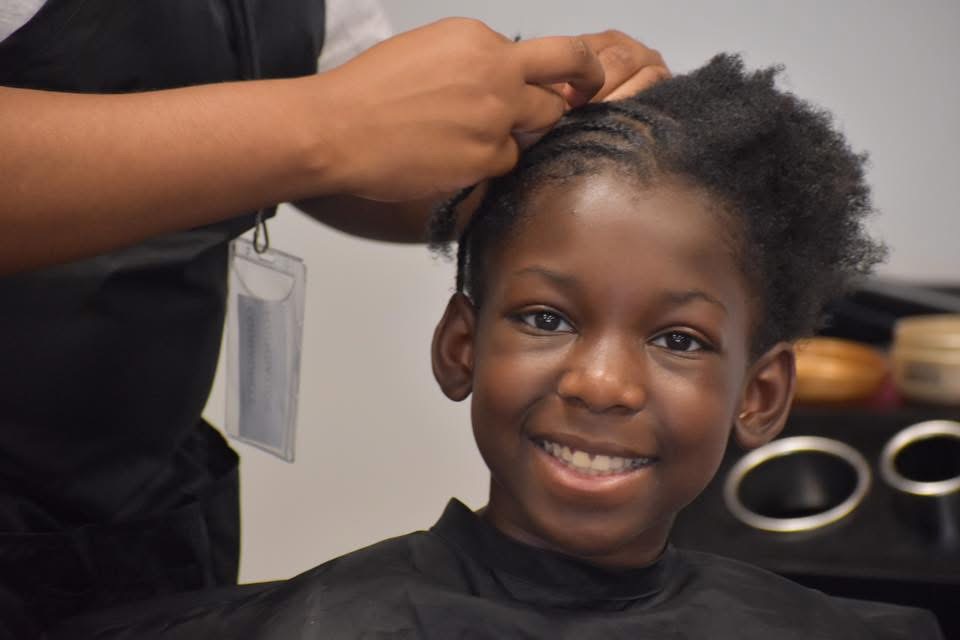 A smiling child has their hair styled at a community event.