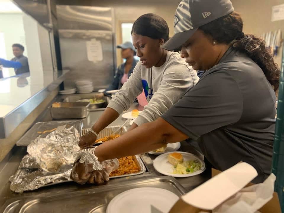 Two Refuge volunteers prepare hot meals together at a serving counter.